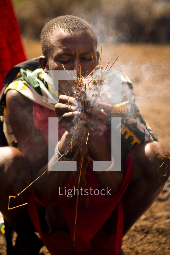 man blowing on embers in a village 