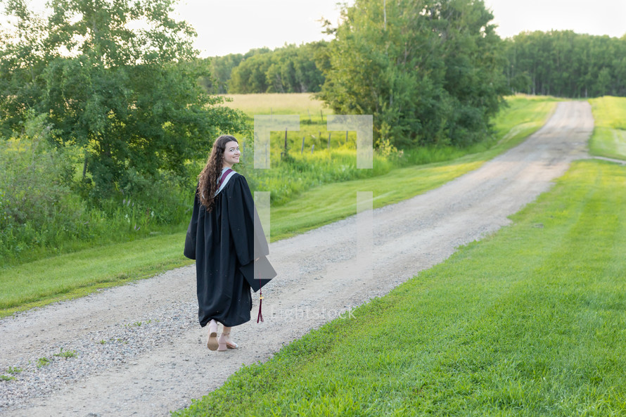 female graduate in cap and gown near a rural field 