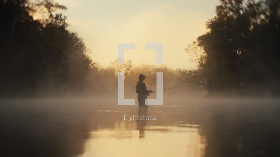 Young fly fisherman casting on a foggy river at sunrise