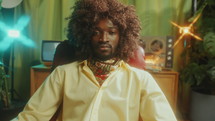 Cool African-American man wearing fashionable outfit and curly hair wig posing at camera with confidence in studio with retro-styled interior. Video portrait
