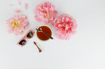 tea cup, pink spring flowers, red lipstick, sunglasses, and spoon against a white background 