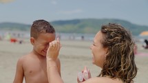 mother applying sunblock lotion on sons skin for sun protection little boy getting ready to swim on the beach with mom using sunscreen caring for childs health on sunny day 
