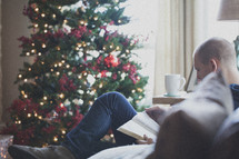 man reading a Bible on a couch in front of a Christmas tree 