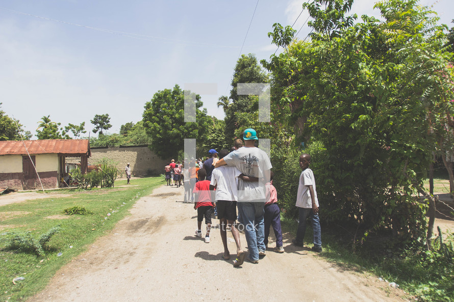 group of people walking on a dirt road in a village 