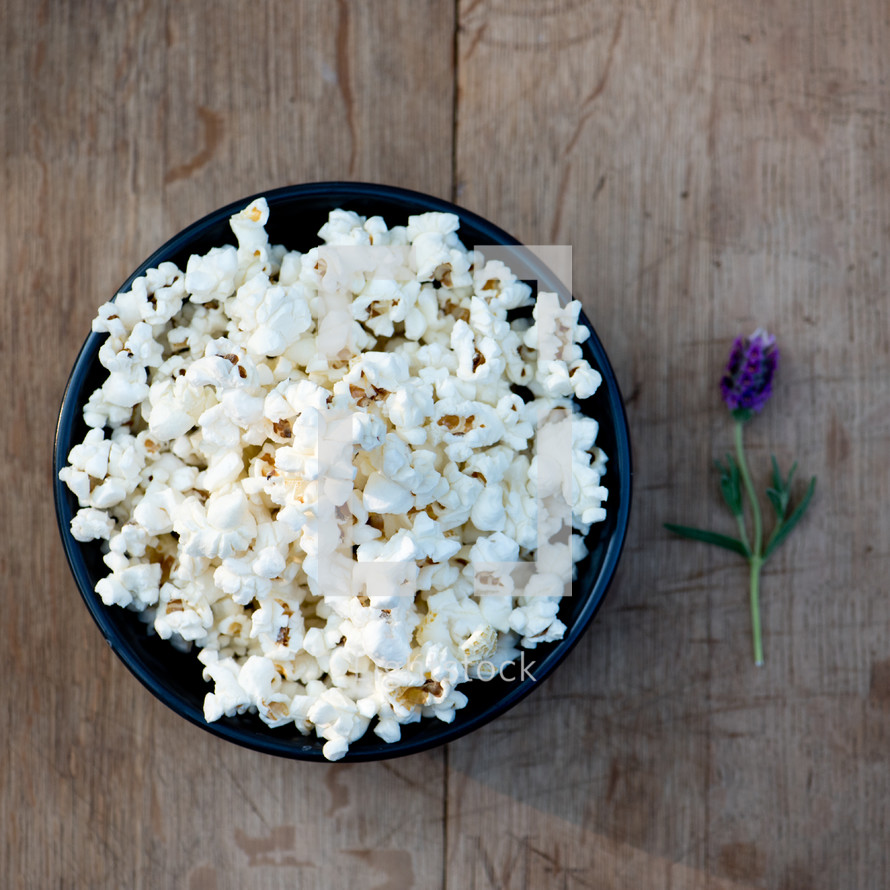 purple flower on a wood background and a bowl of popcorn 