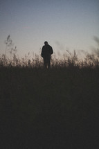 man with his hands in his pockets standing in a field at dusk 