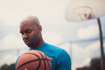 Man in prayer on a basketball court holding a basketball.
