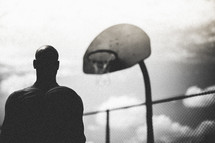 Silhouette of a man standing standing below a basketball hoop.
