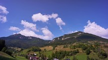 A small village in the valley, the peaks of the Carpathian mountains towering over the village. Fast moving clouds in the blue sky. Summer sunny weather