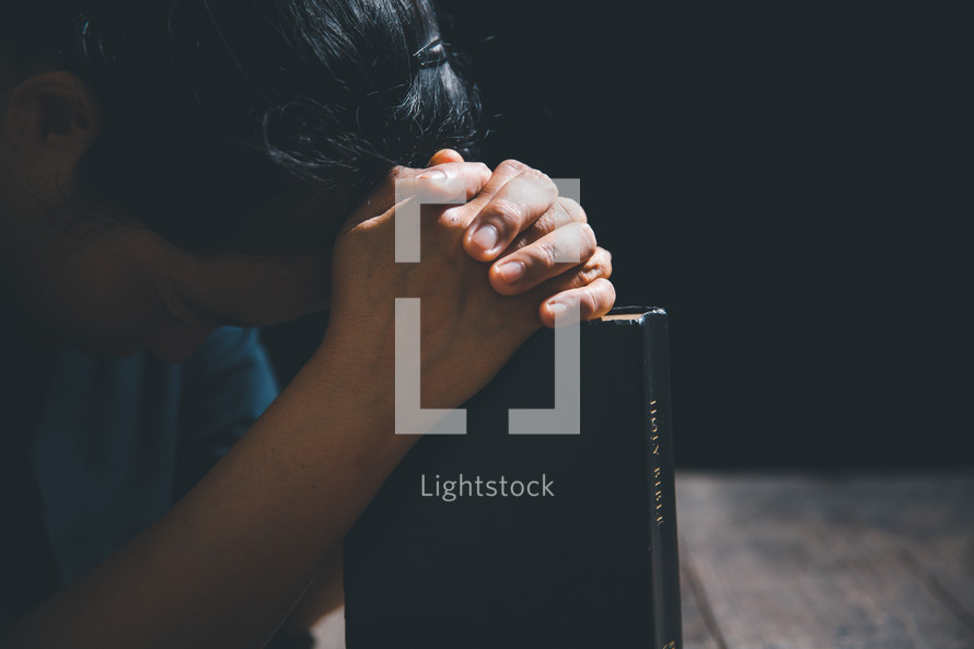 Asian person praying with a bible