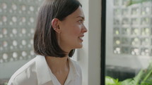 Medium close up shot of young brunette woman in white shirt having conversation with someone while sitting in cafe
