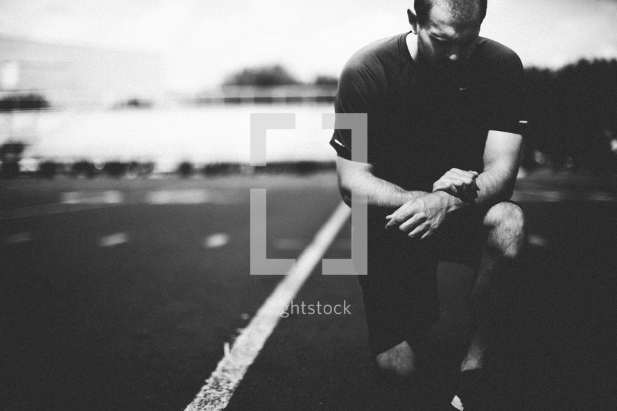 Man kneeling in prayer on a football field.