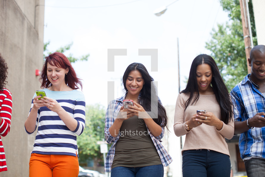 young adults walking down a street checking cellphones 