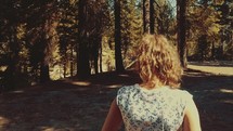 Young girl walks through the woods as camera pans up towards trees