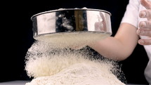 Closeup of female hands sifting flour in slow motion at 180fps on black background.