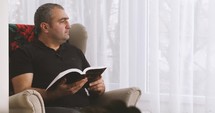 a man sitting in a chair reading a Bible 