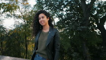 Portrait of happy young latin woman with beautiful curly hair in the street, slow motion. Hispanic girl in black leather jacket smiling and goes to camera. 