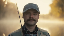 A Smiling young fly fisherman on a foggy river at sunrise