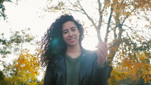 Portrait of happy young latin woman with beautiful curly hair in the street, slow motion. Hispanic girl in black leather jacket smiling and goes to camera.