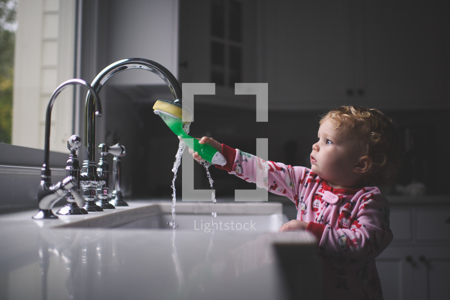 toddler girl playing with a sponge in a kitchen sink 