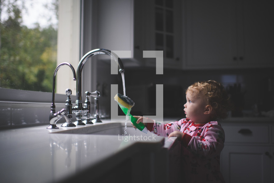 toddler girl playing in a kitchen sink 