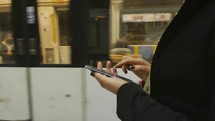 Close up side view of a woman walking and using a smart phone with a subway train moving beside her.