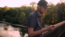 a man on a bridge dialing on a cellphone 