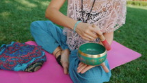 Woman playing singing bowl while sitting on pink yoga mat