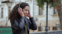 Latin curly haired girl listening music in headphones in autumn park. Beautiful young hispanic lady smiling, singing and enjoying melody outdoor.
