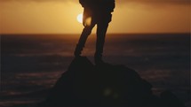 Person standing on a rock facing ocean during sunset - center of frame.
