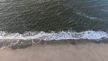Aerial, rising, drone shot above small waves hitting a beach, at the North sea, on Langeoog island, in North Germany
