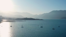 Aerial shot of picturesque lake with ships cruising in the morning, water surface reflecting sunlight and shining, mountains in the background. Potrerillos Dam located in Argentina