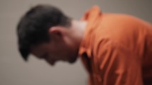 A sad man in orange prison uniform sits in his prison cell.