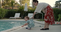 Mother holds back toddler girl as she plays near swimming pool - pool safety