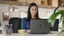 Young female entrepreneur using laptop writing notes stand at home office desk