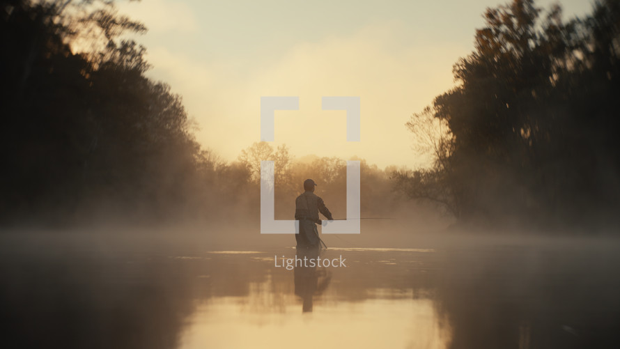 Young fly fisherman casting on a foggy river at sunrise