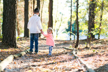 brother and sister holding hands walking on a path outdoors 
