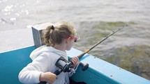 Young Girl Fishing Off Side Of A Blue Boat Sun Shining