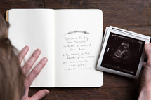 Hand on a card with scripture next to hand holding sonogram images.