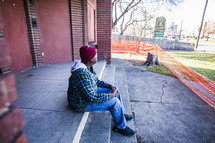 homeless man sitting on stairs in front of a condemned building