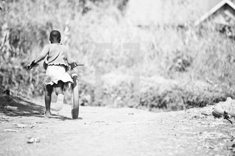 Little African girl running with bike wheel