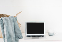 blanket in a basket and laptop computer on a desk 