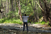 man in a forest with his hands raised in worship to God 