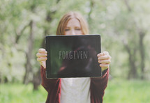 A woman holding out a sign that reads, "Forgiven."