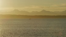 A lone sailboat sails in front of Olympic mountain range in golden hour light