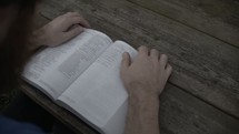 a man sitting at a picnic table reading a Bible outdoors 
