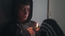 Young teenage boy lights and smokes a cigarette or marijuana joint.