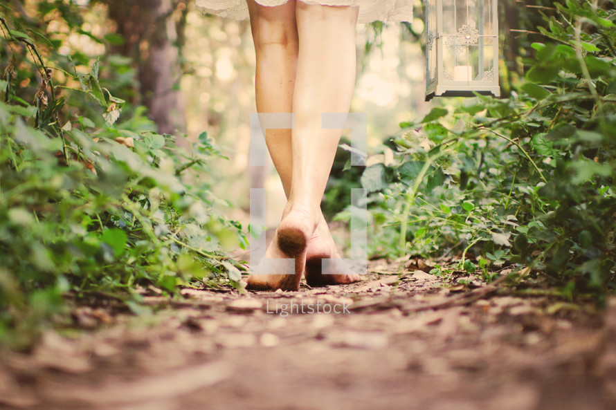 dirty feet of a woman walking barefoot on a dirt path carrying a lantern 