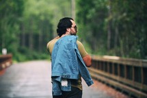 a man walking outdoors with a denim jacket over his shoulders 