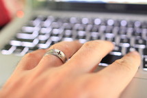cross on a wedding band and hand on a keyboard 